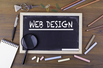 Web Design. Text on the chalk board. Wooden table with a magnifying glass and writing utensils.