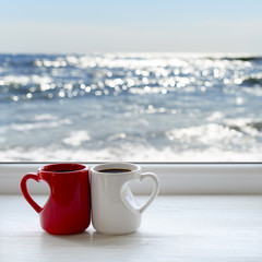 Two cups of hot tea on a windowsill. In the background sea and sky