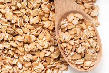 Oat flakes in wooden spoon and on white background. Close up, top view, high resolution product