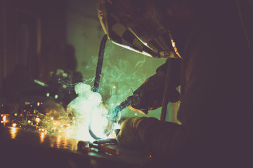 Fototapeta premium Industrial worker welding a loop made of round pipe on work table, producing smoke, sparks and reflections