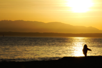 Fototapeta na wymiar Silhouette of a baby girl playing on the beach at sunset: Golden Gardens Park, Seattle (US)