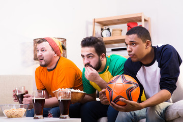 Image of friends waiting for funny or emotional moments while watching football game on TV. Hnadsome men drinking beer and eating pop corn.