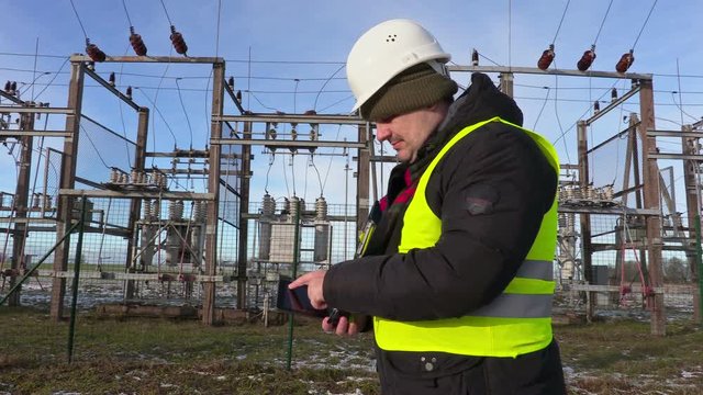 Electrician engineer using tablet near substation in winter
