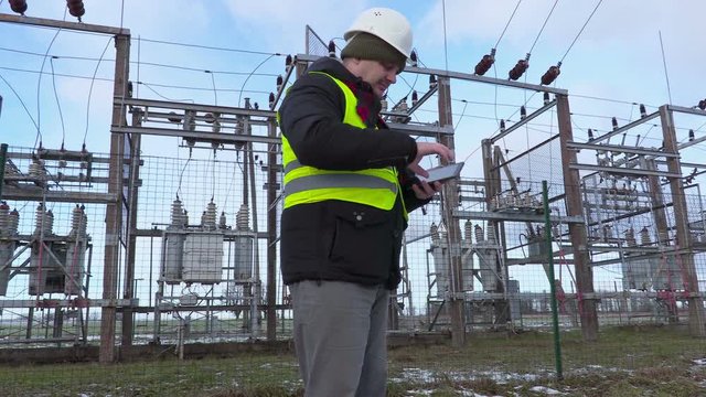 Electrician engineer take pictures on tablet near substation in winter