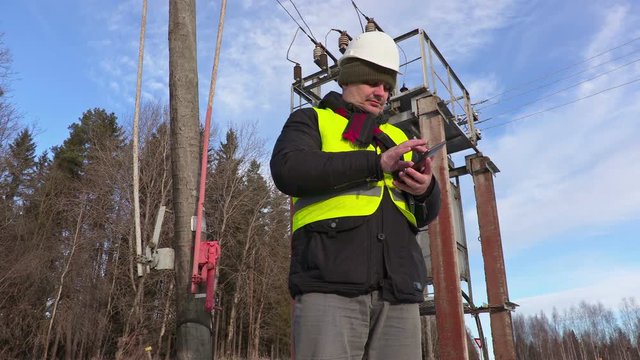 Electrician engineer using tablet near power lines and transformer