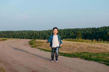 Obraz premium 3-4 years little boy runs along a country road, happy, laughing. The sky and the coniferous forest on the horizon. Summer time