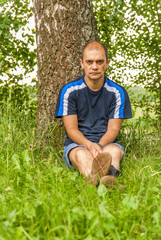 Naklejka na ściany i meble a man is sitting on the grass near a tree 