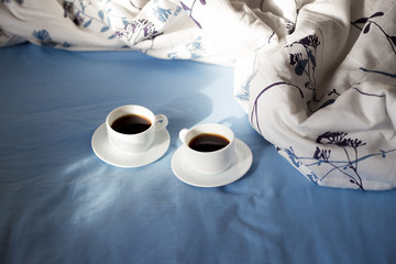 Two white cups of coffee are in bed, sunny morning
