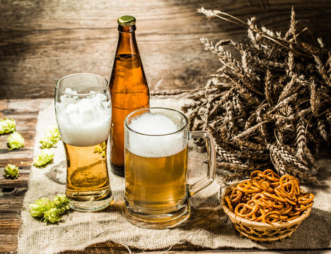 Mug, glasse, bottle of beer with foam on cloth and pretzels