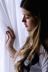Teenage girl looking through a window, inside a house