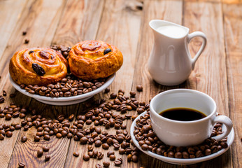 Coffee cup with milk jug and cinnabons on wooden background.