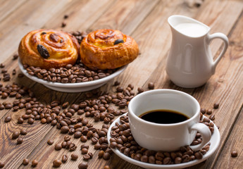 Coffee cup with milk jug and cinnabons on wooden background.