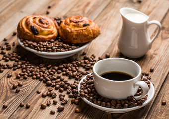 Coffee cup with milk jug and cinnabons on wooden background.