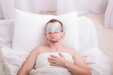 Sleeping young man in sleep mask on bed.