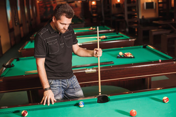 Concentrated player with a cue in billiard room.