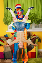 Clown holds the little girl head over heels.