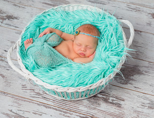 lovely sleeping newborn girl in round cot with turquoise blanket