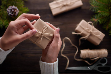 Beautiful female hands are packed Christmas gift in brown kraft paper.