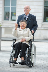Fototapeta na wymiar senior man pushing woman in wheelchair in the city