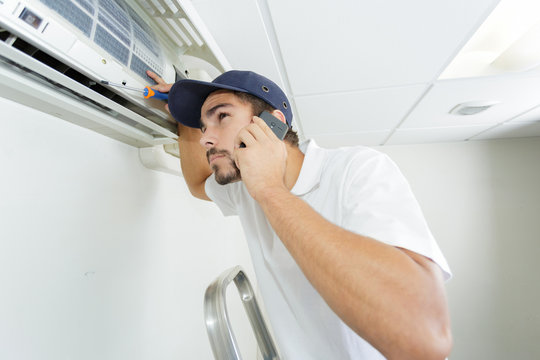 young handyman repairing air conditioning system calling for help