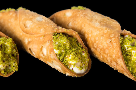 Traditional sicilian canoli with ricotta and mascarpone cream decorated with pistachio on a black background