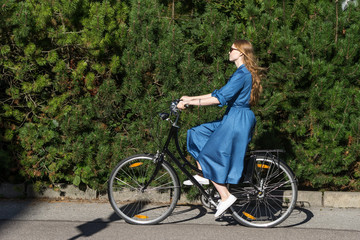 Fototapeta premium Beautiful young woman and vintage bicycle, summer. Red hair girl riding the old black retro bike outside in the park. Having fun in the city