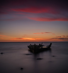 Old broken boat wreck on the shore, a frozen sea and beautiful red sunset background. Estonia, Europe.