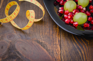 fitness concept with pomegranate, grapes in black plate and centimeter/fitness background with pomegranate, grapes in black plate and centimeter