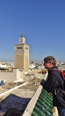 A tourist on a rooftop in the Medina of Tunis: View of the Al-Zaytuna Mosque Minaret and the...