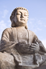 Portrait of Buddha image in lotus position on sky background.