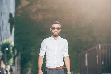 Young handsome modern businessman posing leaning against a wall, overlooking left, wearing a coat - business, success concept