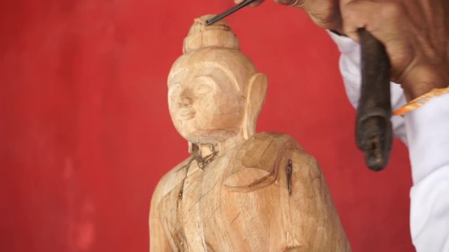Man carves a statue of Buddha made of wood