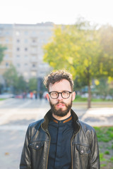 Portrait of young handsome caucasian bearded businessman posing outdoor in the street, looking at camera pensive wearing glasses - business, thoughtful, serious concept