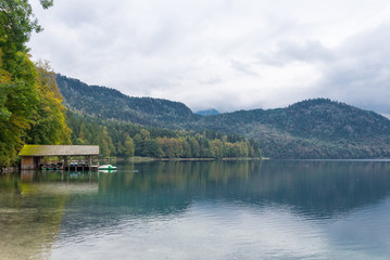 Small wood cabin on a shore of the beautiful lake name Alpsee in Bavaria, Germany during cloudy sky.