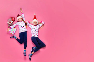 Two sisters lying on the floor on a pink background in pajamas 