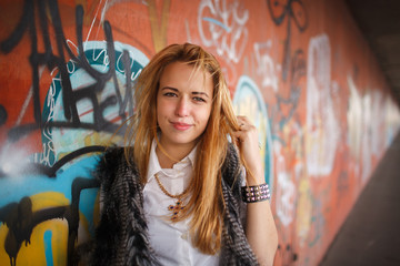 Russian beautiful smiling teenager girl with long blond hair and make up near the wall  graffiti, selective focus