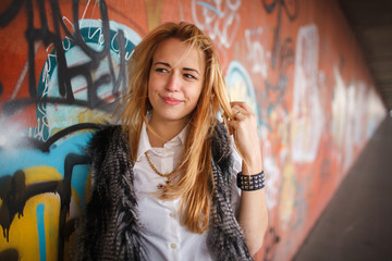 Russian beautiful smiling teenager girl with long blond hair and make up near the wall  graffiti, selective focus