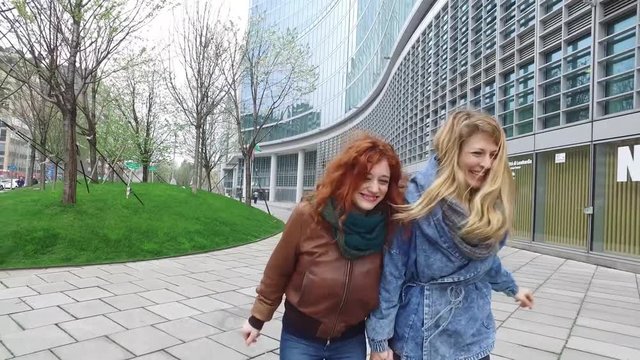 Two young beautiful caucasian blonde and redhead women friends running outdoor in the city having fun - friendship, relaxing, having fun concept