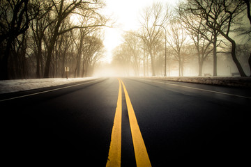 Yellow dividing lines on asphalt road toward bright morning light