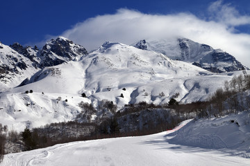 Ski slope and mountains in clouds at sunny day