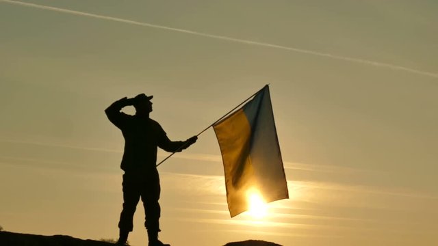 4K. Soldier silhouette salute Ukrainian Flag, sunrise time  