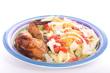 Colorful salad with chicken thigh and wing on the side, on plate with light background