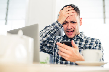 Fototapeta premium Closeup portrait, stressed young man in purple sweater, shocked surprised, horrified and disturbed, by what he sees on his cell phone, isolated indoors background.