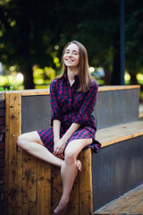 Girl wearing checkered dress sitting down in skatepark looking at camera.