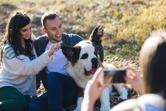 Woman takes a photo of young couple enjoying together with their Saint Bernard puppy .