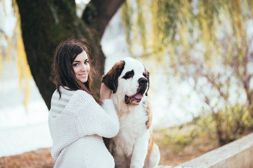 Beautiful young brunette woman sitting next to her adorable Saint Bernard puppy in park.