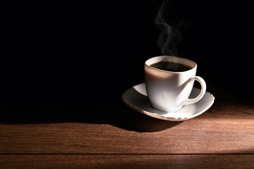 White cup of hot coffee on the table and a dark background