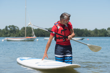 man next to a stand-up paddle board on the lake