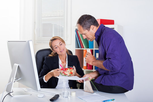 couple souriant au bureau qui mange en travaillant