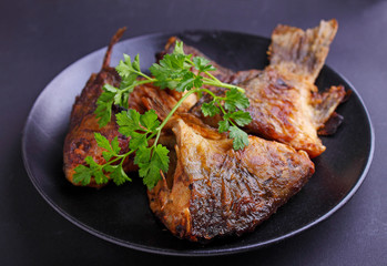 Fried fish on a black plate decorated with fresh parsley on a black background